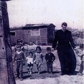 Foto de archivo: el padre Leoncio caminando de la mano con niños del barrio frente a una casilla de madera